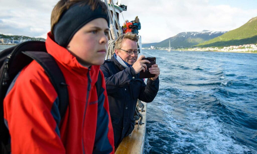 Gutt med lue og far ser utover sjøen fra rekka på Hermes II utenfor Tromsø