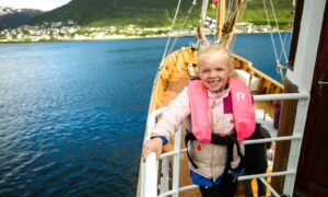 Jente i redningsvest står ved rekka om bord på Hermes II med Tromsø i bakgrunnen