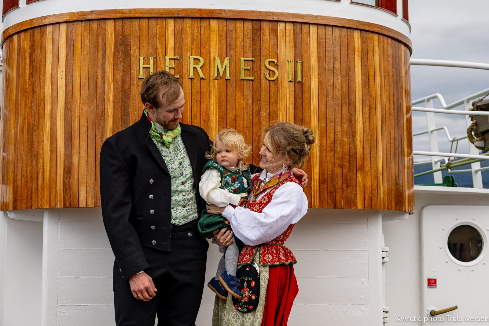 A wedding couple in traditional bunad by the nameboard of Hermes II in Tromsø